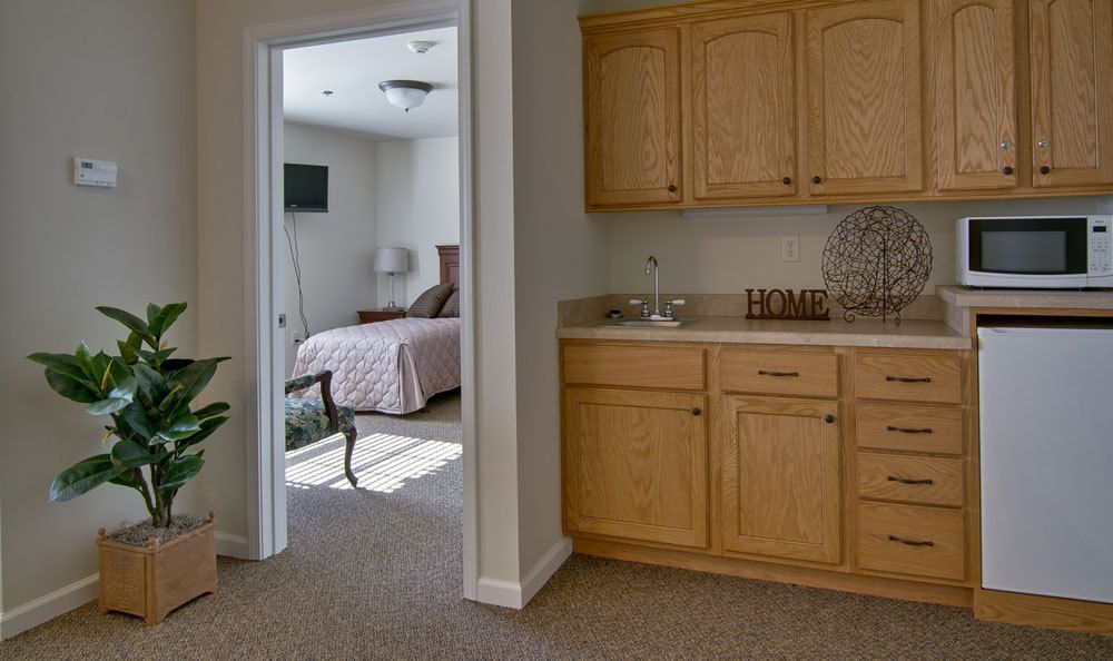 A cozy interior featuring a kitchenette and a bedroom with sunlight streaming in.