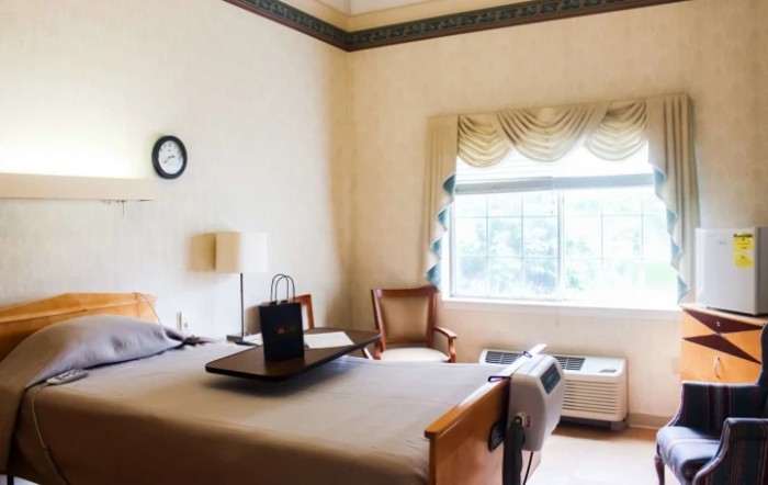 A clean and well-lit hospital room with a bed and seating area by the window.