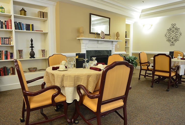 An elegant dining room with a beautifully set table, surrounded by upholstered chairs and a fireplace with a mirror above it.