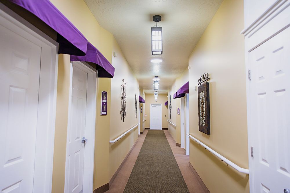 A brightly lit hallway with multiple doors on each side, decorated with purple accents and framed art.