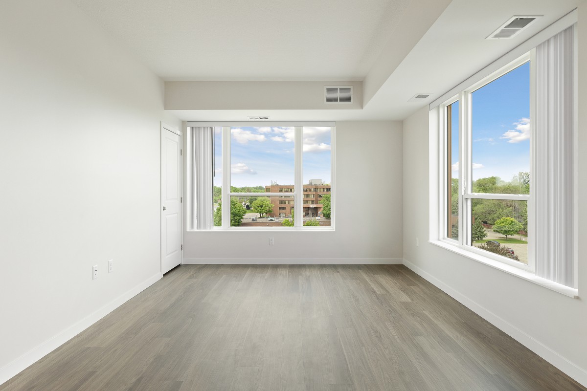 A bright, empty room with large windows and hardwood flooring.