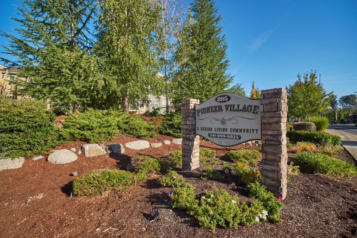 A landscaped property entrance featuring a sign for Windsor Village, surrounded by trees and greenery.