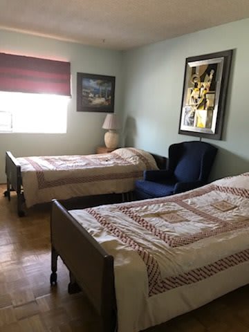A cozy bedroom featuring two twin beds, a window with blinds, and decorative items on the walls.