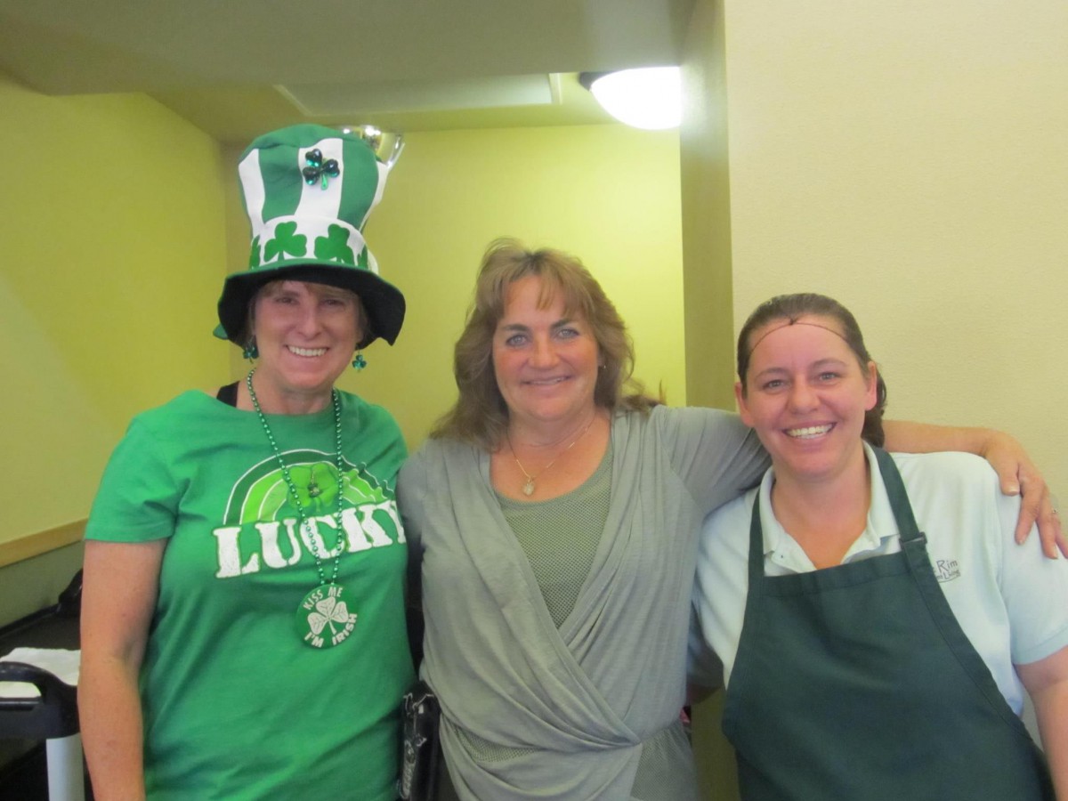 Three people smiling, one wearing a festive St. Patrick's Day hat.