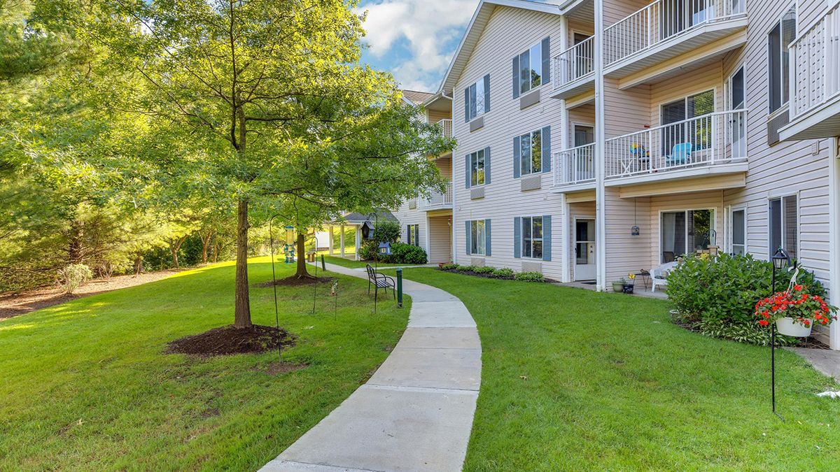 A modern apartment building with balconies, surrounded by lush greenery and a winding pathway.