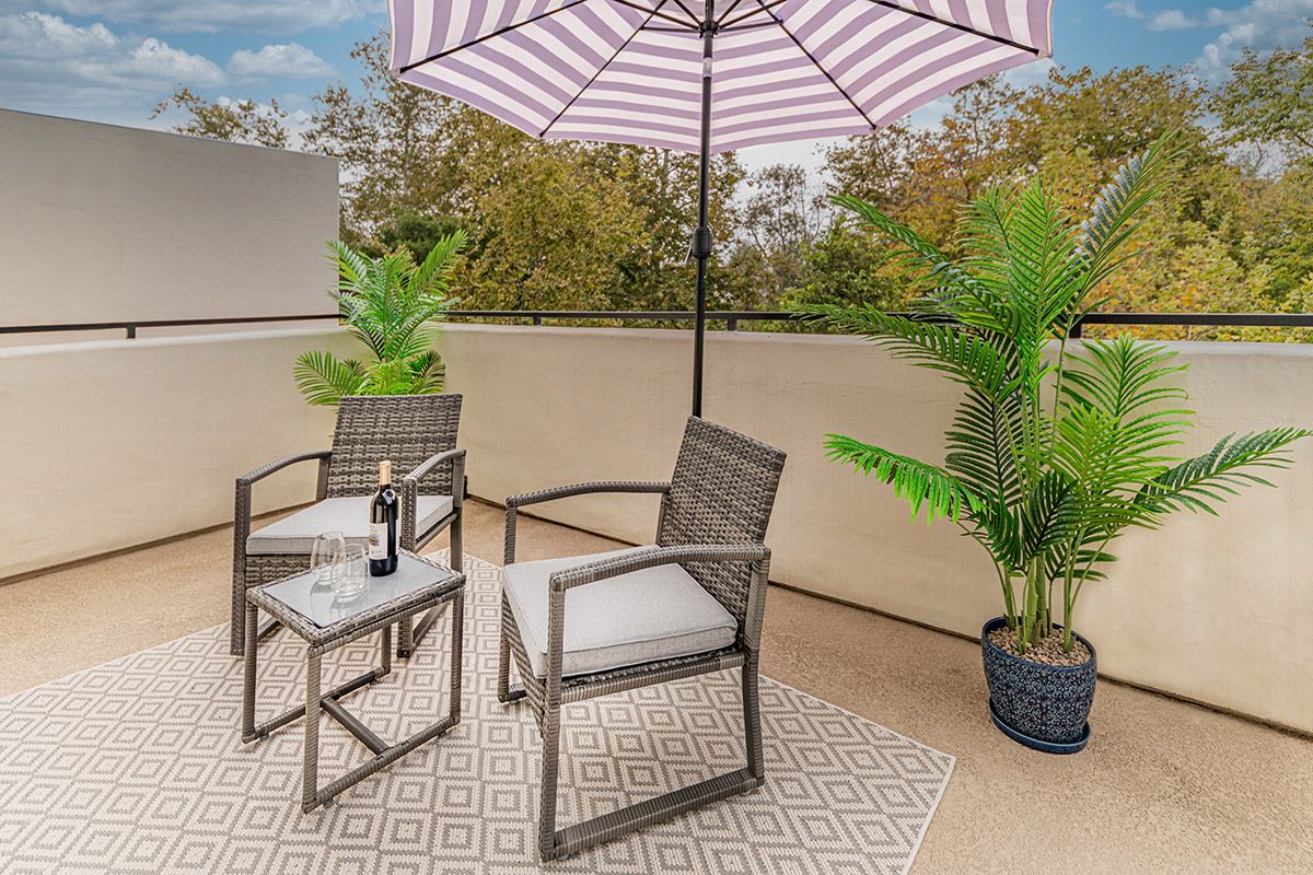 A cozy patio setup with chairs and a table under an umbrella, surrounded by potted plants.