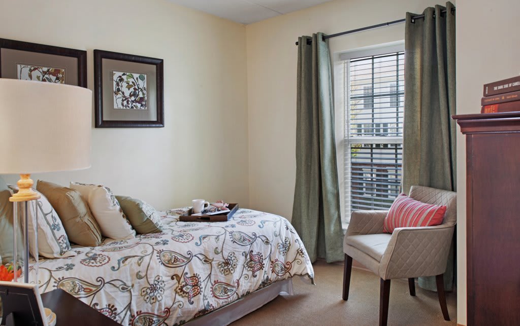 A cozy bedroom with a single bed, decorative pillows, and a comfortable chair by the window.