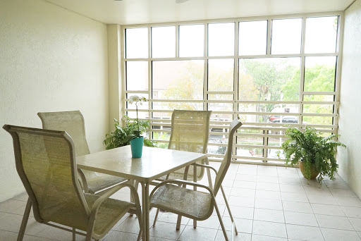 A bright and airy sunroom featuring a simple dining setup with chairs and a table surrounded by greenery.