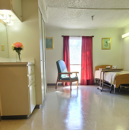 A spacious and well-lit hospital room featuring a bed, chair, and decorative flowers.