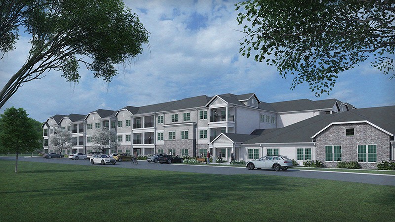 A residential apartment building with a parking lot in front, surrounded by trees and grass under a cloudy sky.