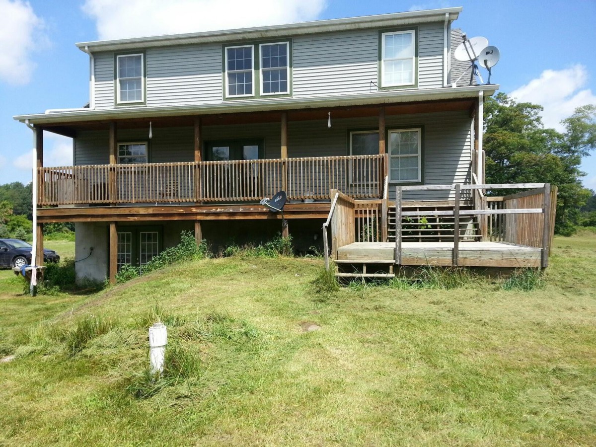 A two-story house with a wooden deck and a grassy lawn.