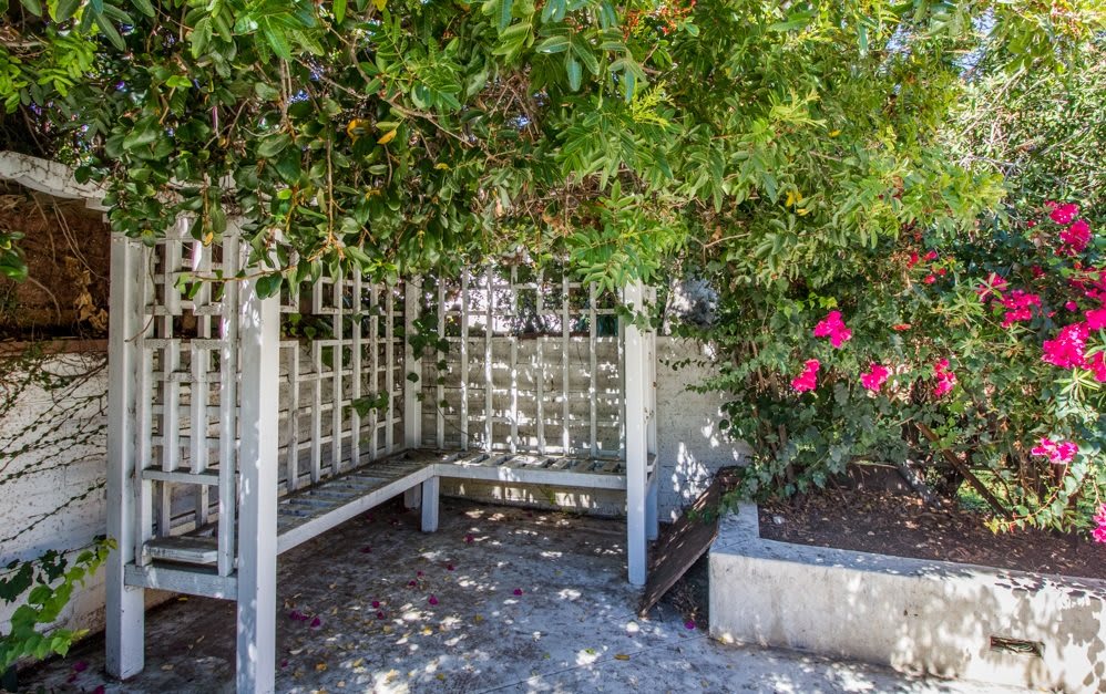 A quiet garden corner featuring a wooden bench surrounded by lush foliage and vibrant flowers.