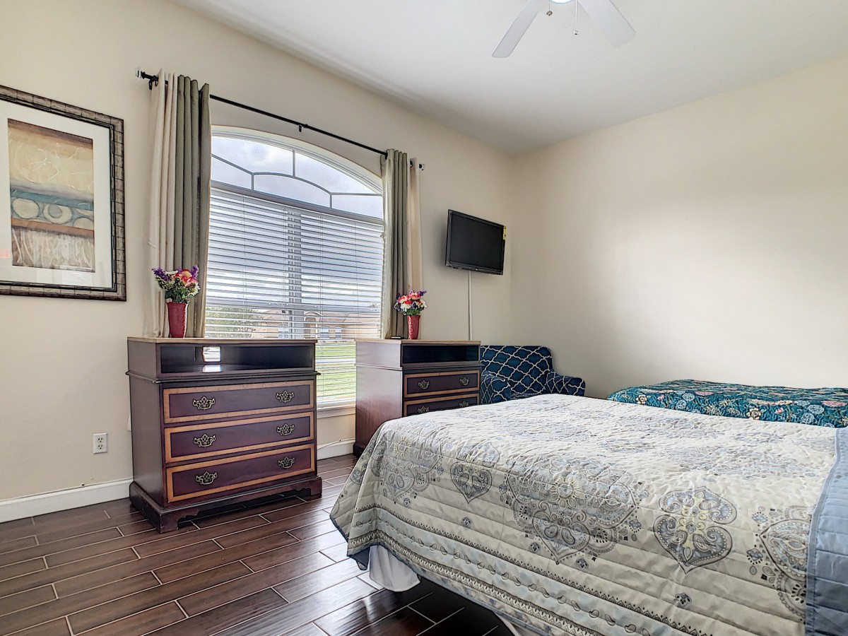 A cozy bedroom with a bed, dresser, television, and large window.