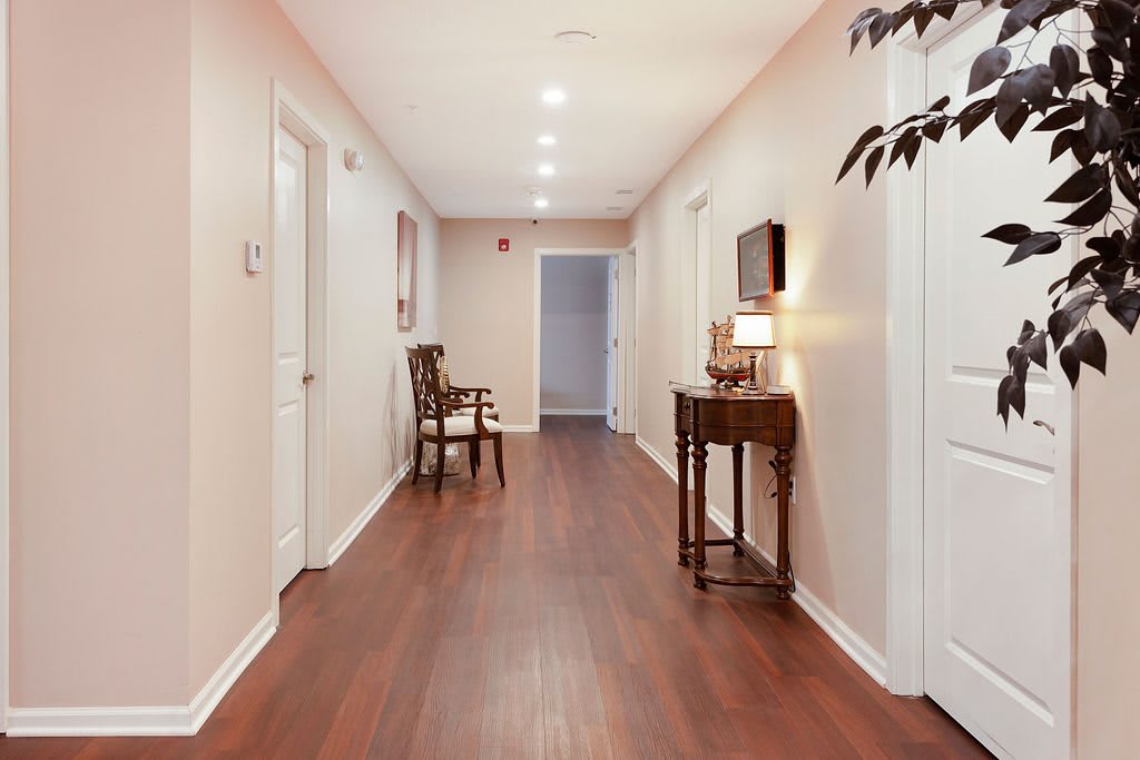 A well-lit hallway with wooden flooring, featuring a chair and a small table with a lamp.