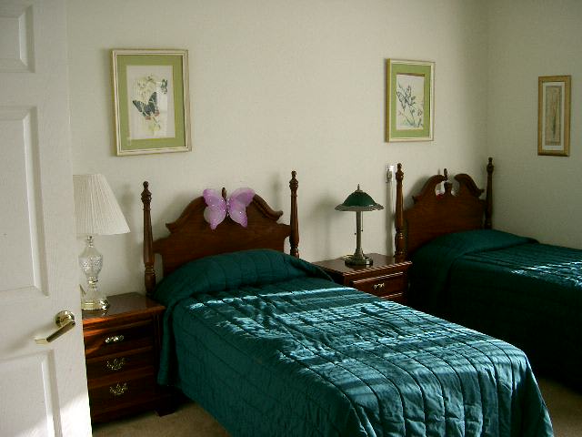 A traditional bedroom with twin beds featuring green bedding, complemented by a nightstand and two framed artworks on the wall.