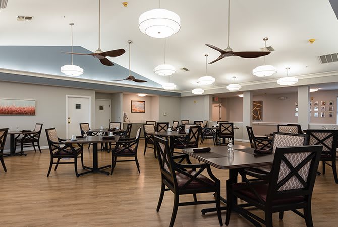 A well-lit dining area with wooden tables and chairs arranged neatly under ceiling fans.