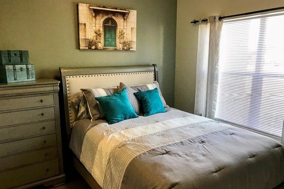 A cozy bedroom with a neatly made bed, featuring turquoise pillows and wall art above the headboard.