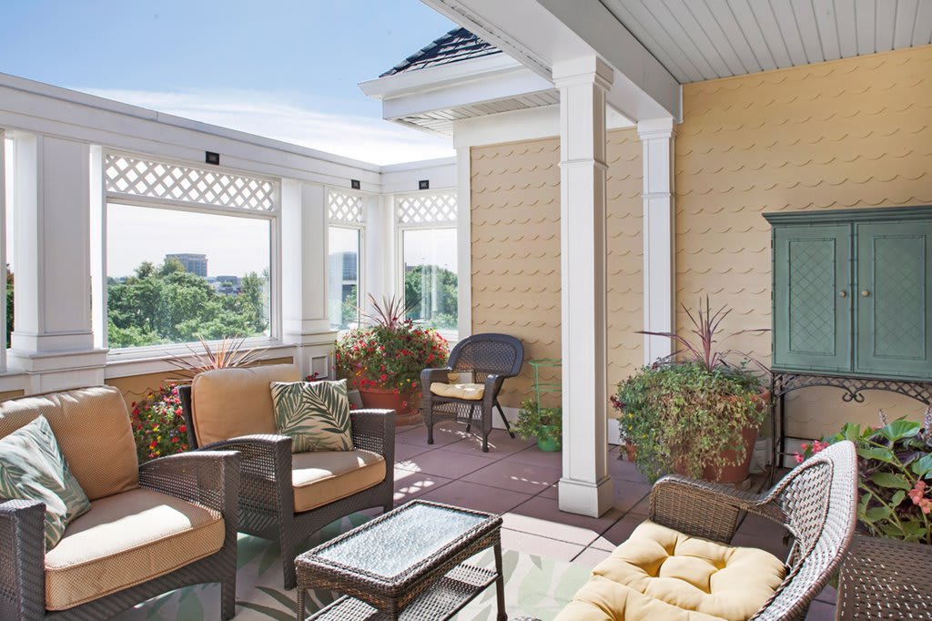 A cozy patio with comfortable seating, surrounded by plants and large windows.
