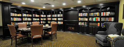 A cozy library setting featuring comfortable seating, a fireplace, and well-stocked bookshelves.
