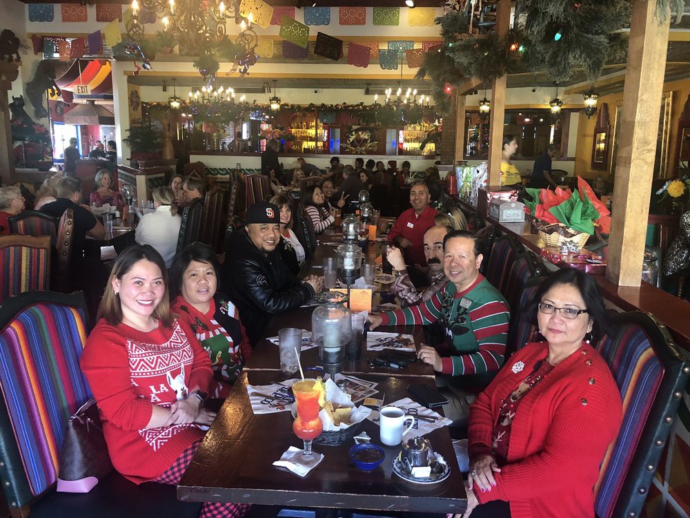 A festive group enjoying a holiday meal at a restaurant, wearing Christmas-themed attire.