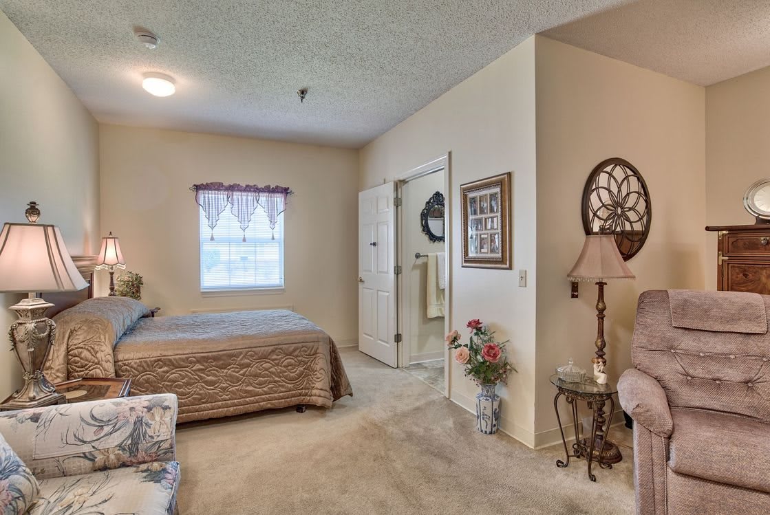 A cozy bedroom with a neatly made bed, a standing lamp, and decorative elements.