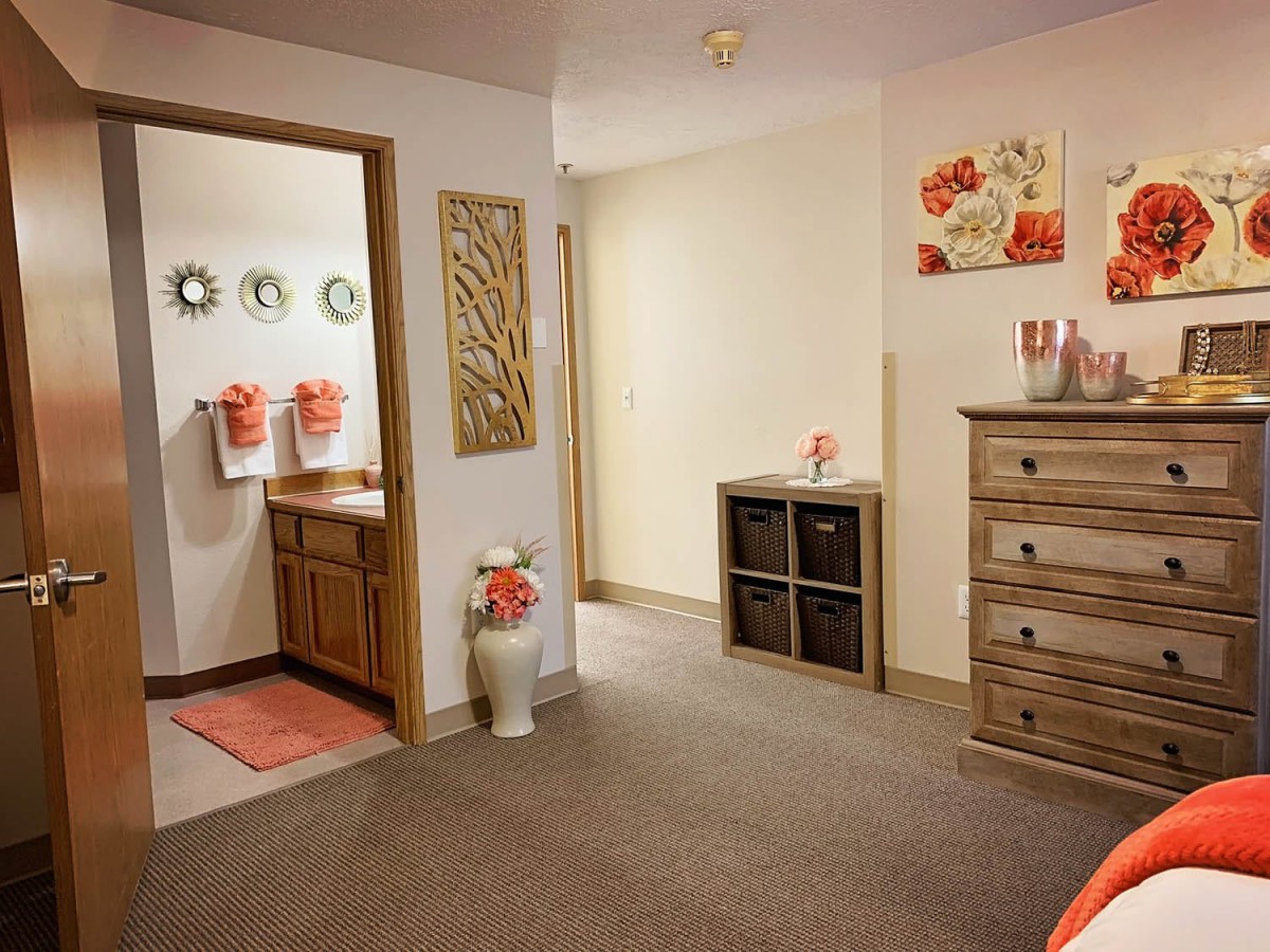 Cozy interior view of a bedroom leading to a bathroom, featuring warm decor and wooden furniture.