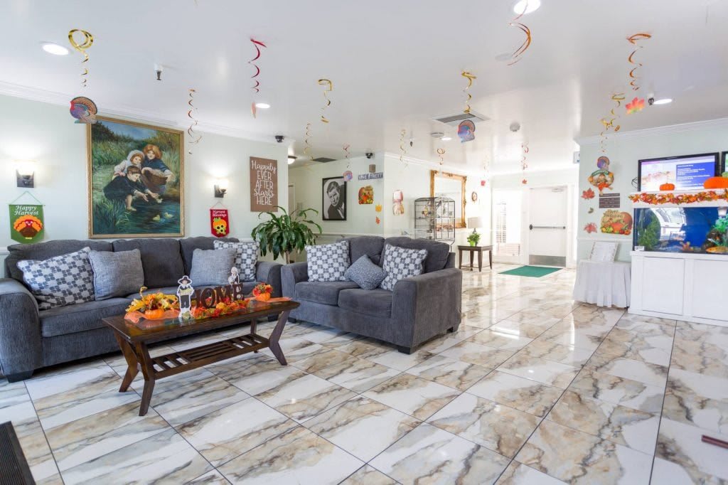 A well-decorated living room featuring gray sofas, a wooden coffee table with decorative items, marble flooring, and vibrant artwork.