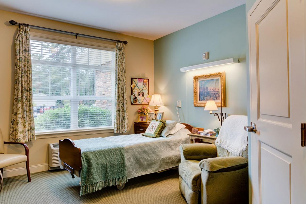 A cozy bedroom with a large window, featuring an armchair and artwork on the walls.