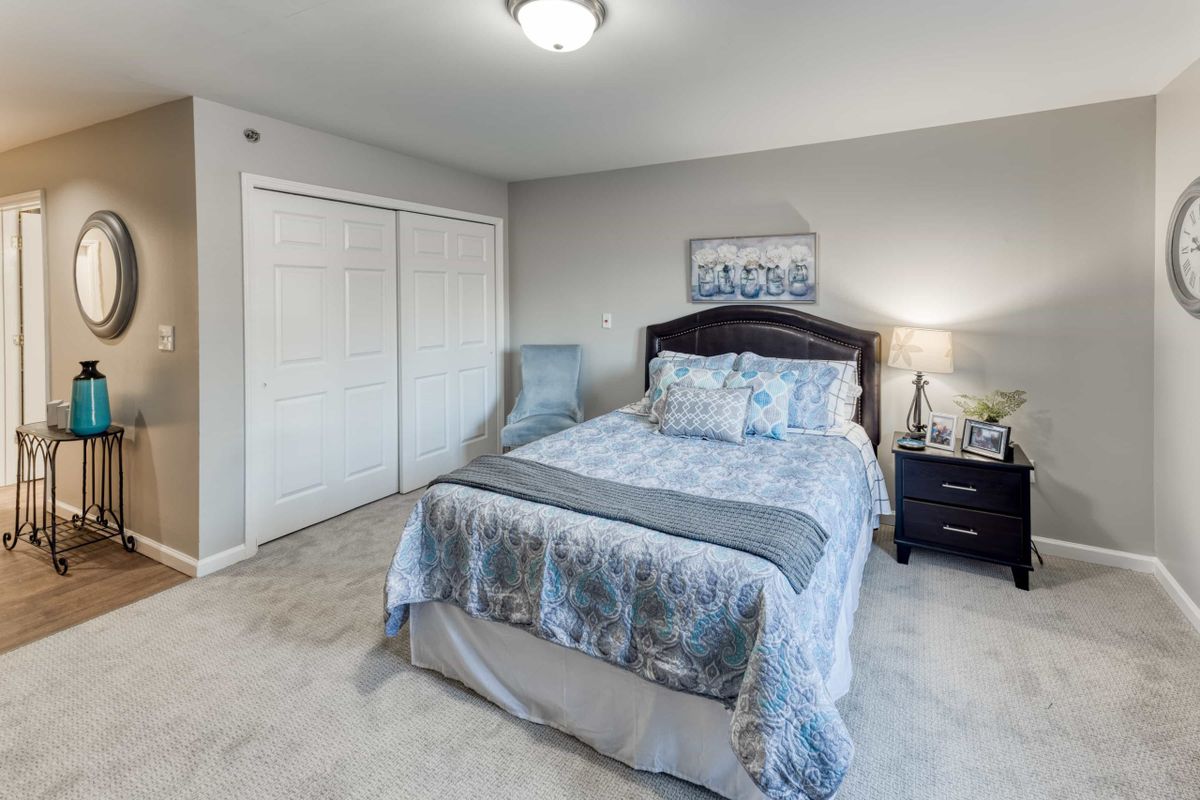 A well-appointed bedroom featuring a neatly made bed with patterned bedding, a nightstand with a lamp, and a closet with sliding doors.