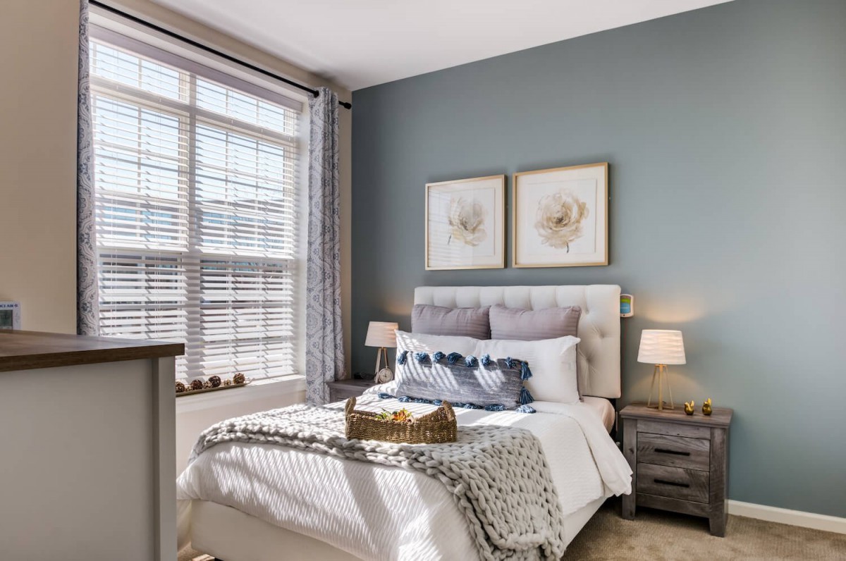 A cozy bedroom with elegant decor, featuring a bed with plush pillows and soft lighting, enhanced by natural light through a large window.
