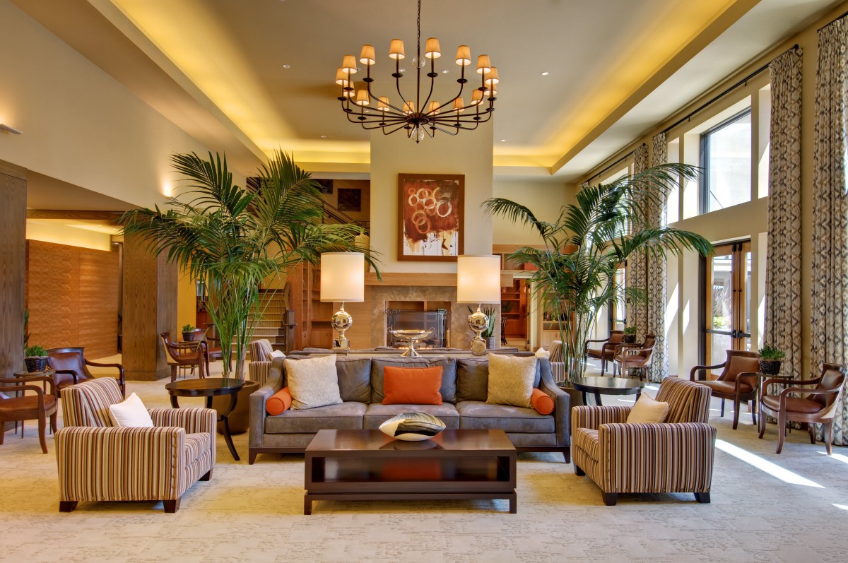 A stylish and modern living room featuring elegant furniture, a large chandelier, and lush indoor plants.