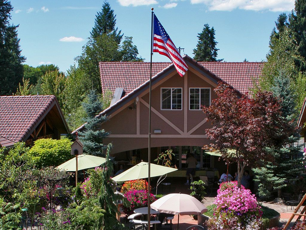 A house with a garden patio adorned with an American flag and surrounded by trees and outdoor seating arrangements.