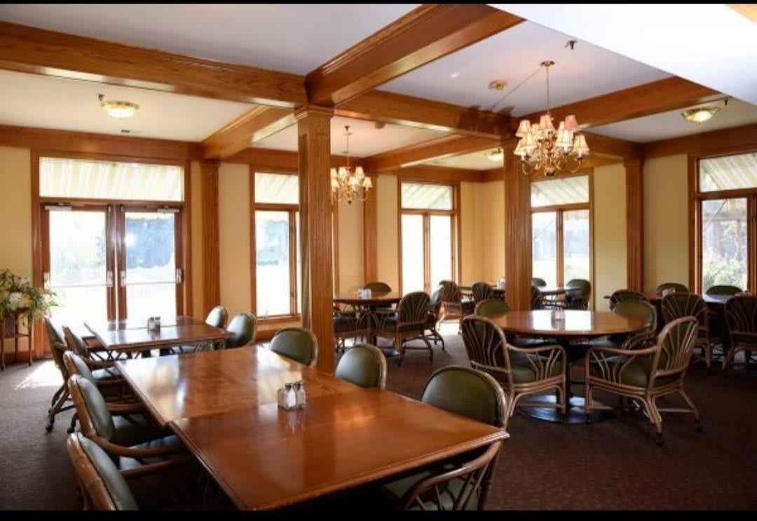An elegant dining area with wooden furniture and chandeliers, illuminated by natural light.