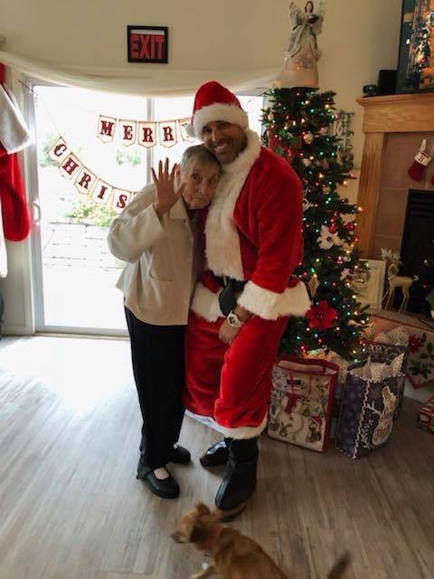 A cheerful person dressed as Santa Claus poses with an elderly woman in a festive Christmas setting.