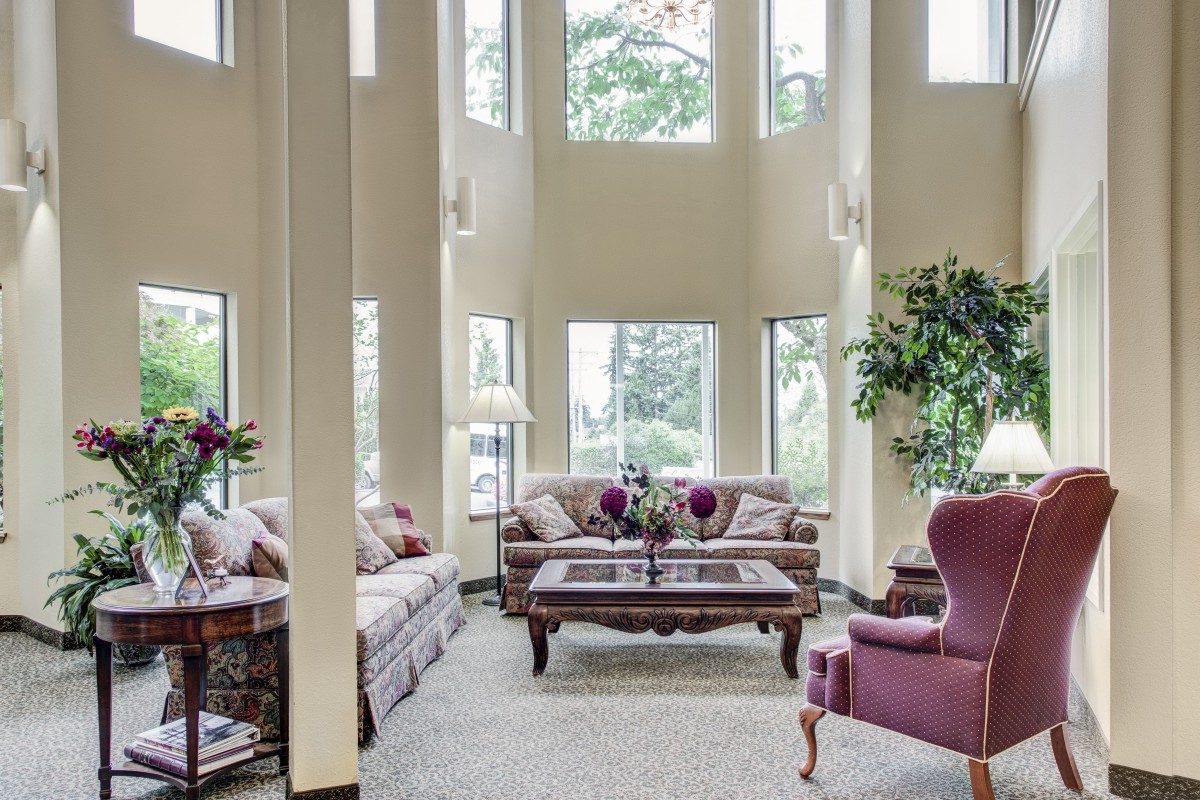A spacious living room with tall windows, elegant furniture, and indoor plants.