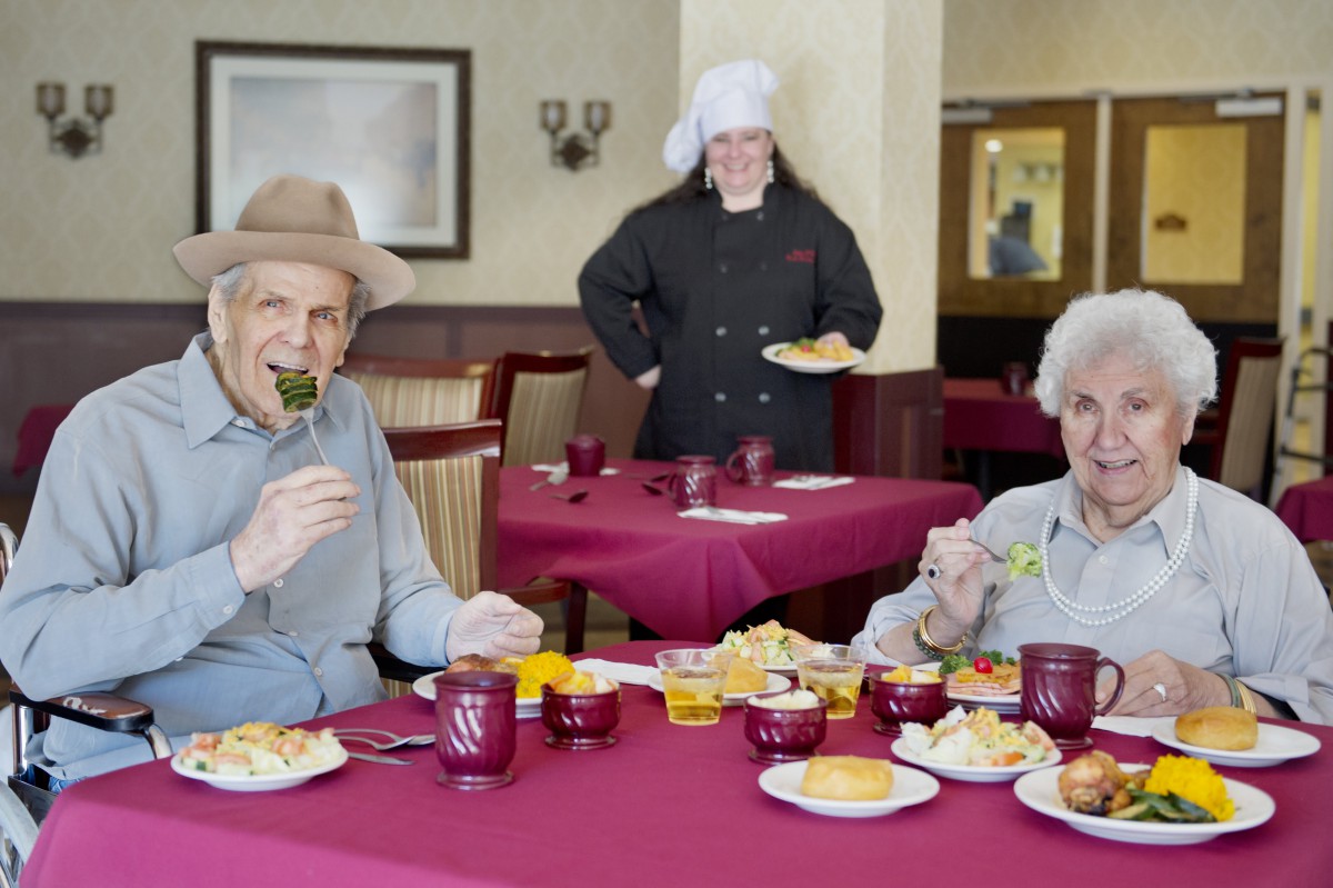 Elderly individuals enjoying a meal at a restaurant, with a chef in the background.