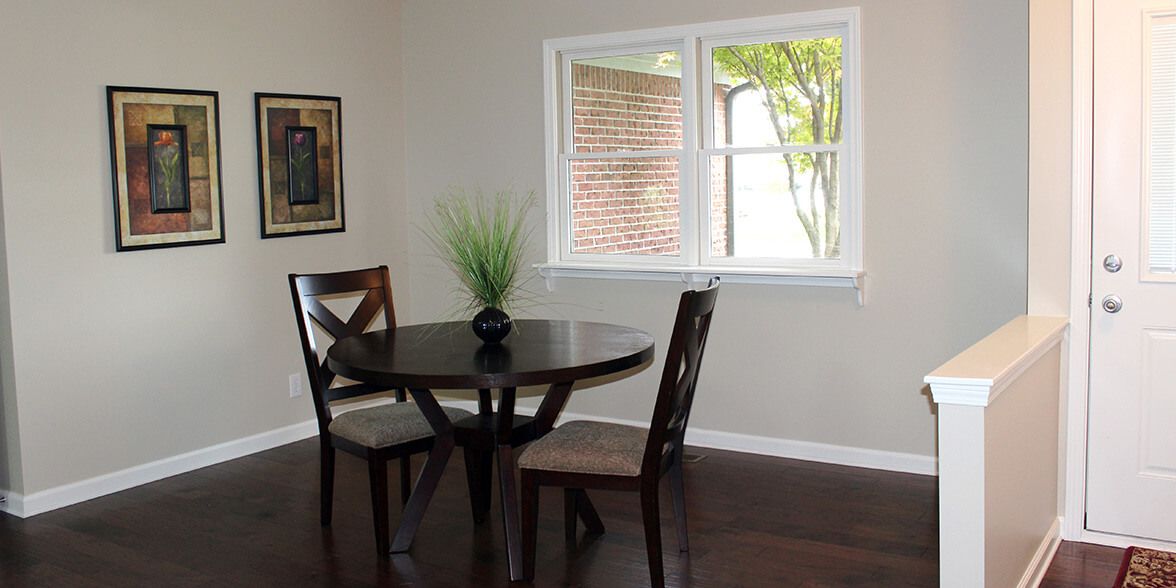 A small dining area with a round table and two chairs beside a window, featuring minimalist decor.