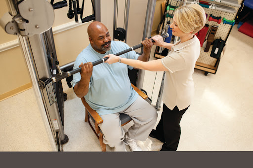 A personal trainer assists a client with strength training in a rehabilitation setting.