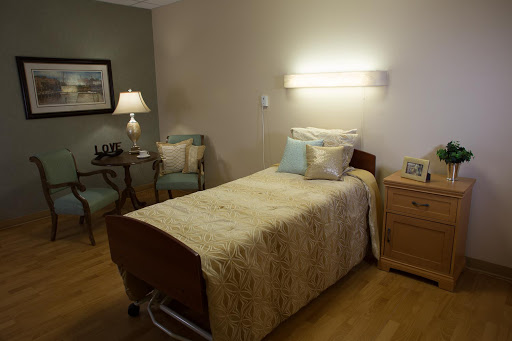 A well-furnished hospital room with a bed, seating area, and soft lighting.