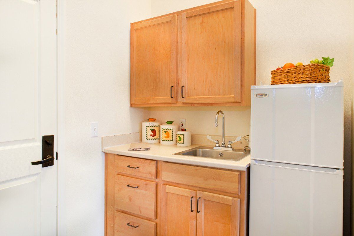 A small kitchen area with wooden cabinets, a sink, countertop, and storage jars next to a refrigerator.