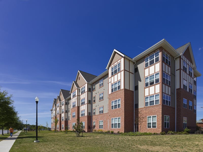 A modern multi-story apartment building with a brick and siding exterior under a clear blue sky.