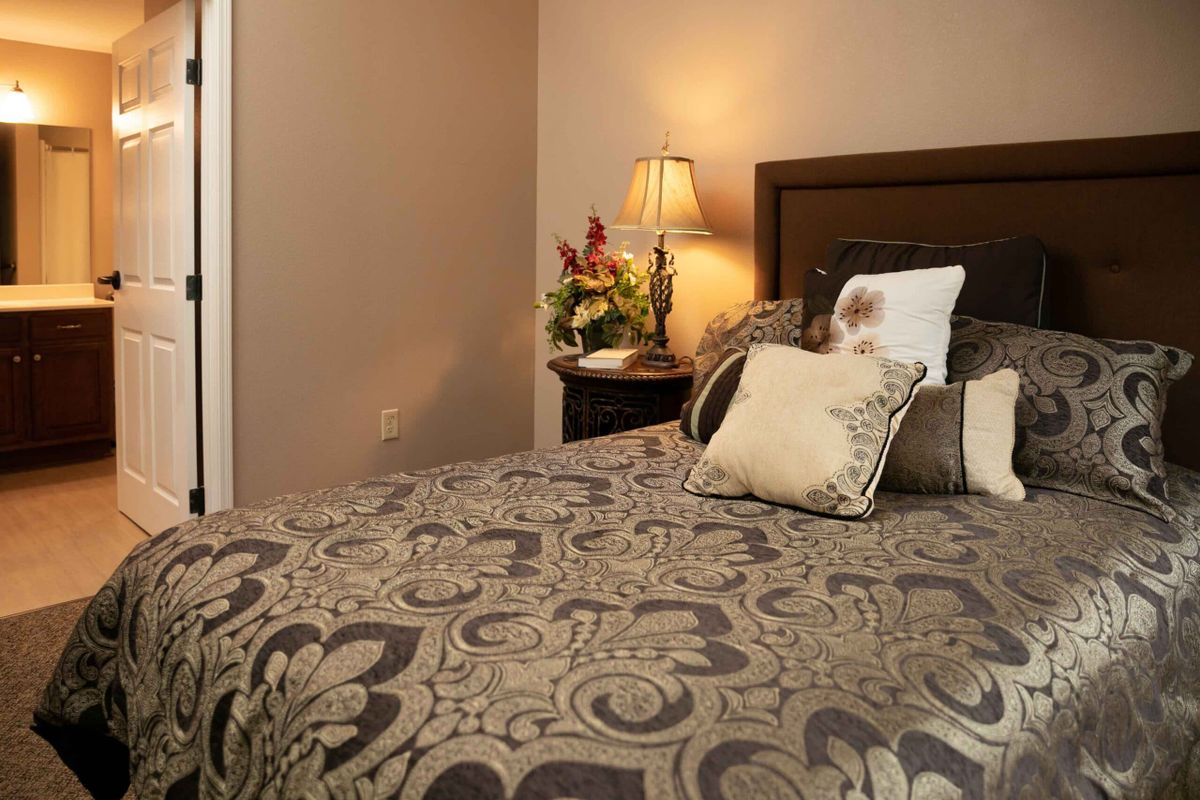 A cozy bedroom with patterned bedding and a bedside lamp illuminating a vase of flowers.