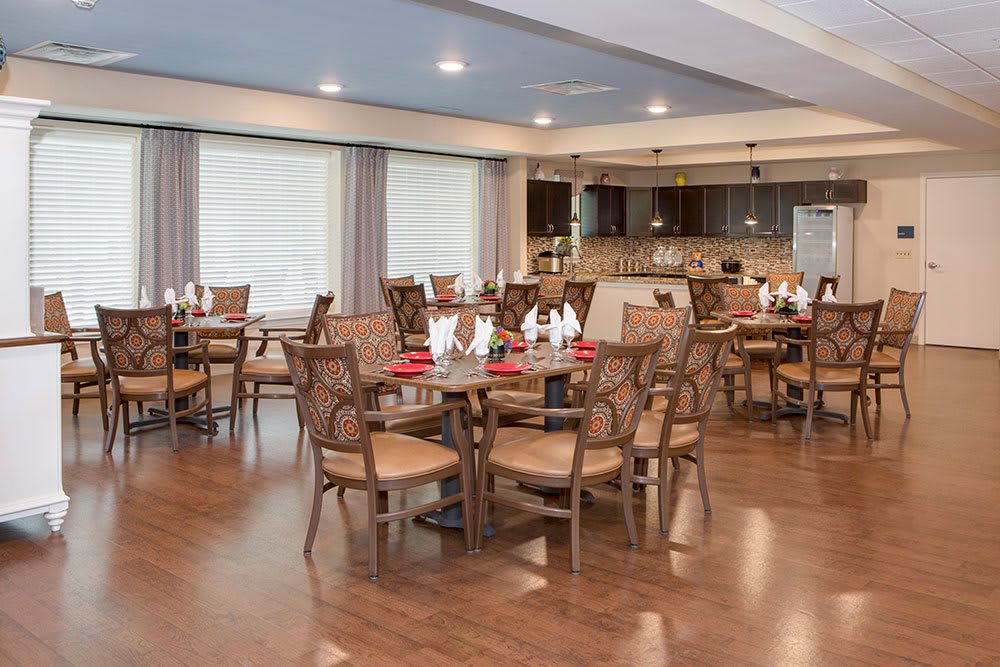 A spacious dining room with elegantly set tables and a modern kitchen in the background.
