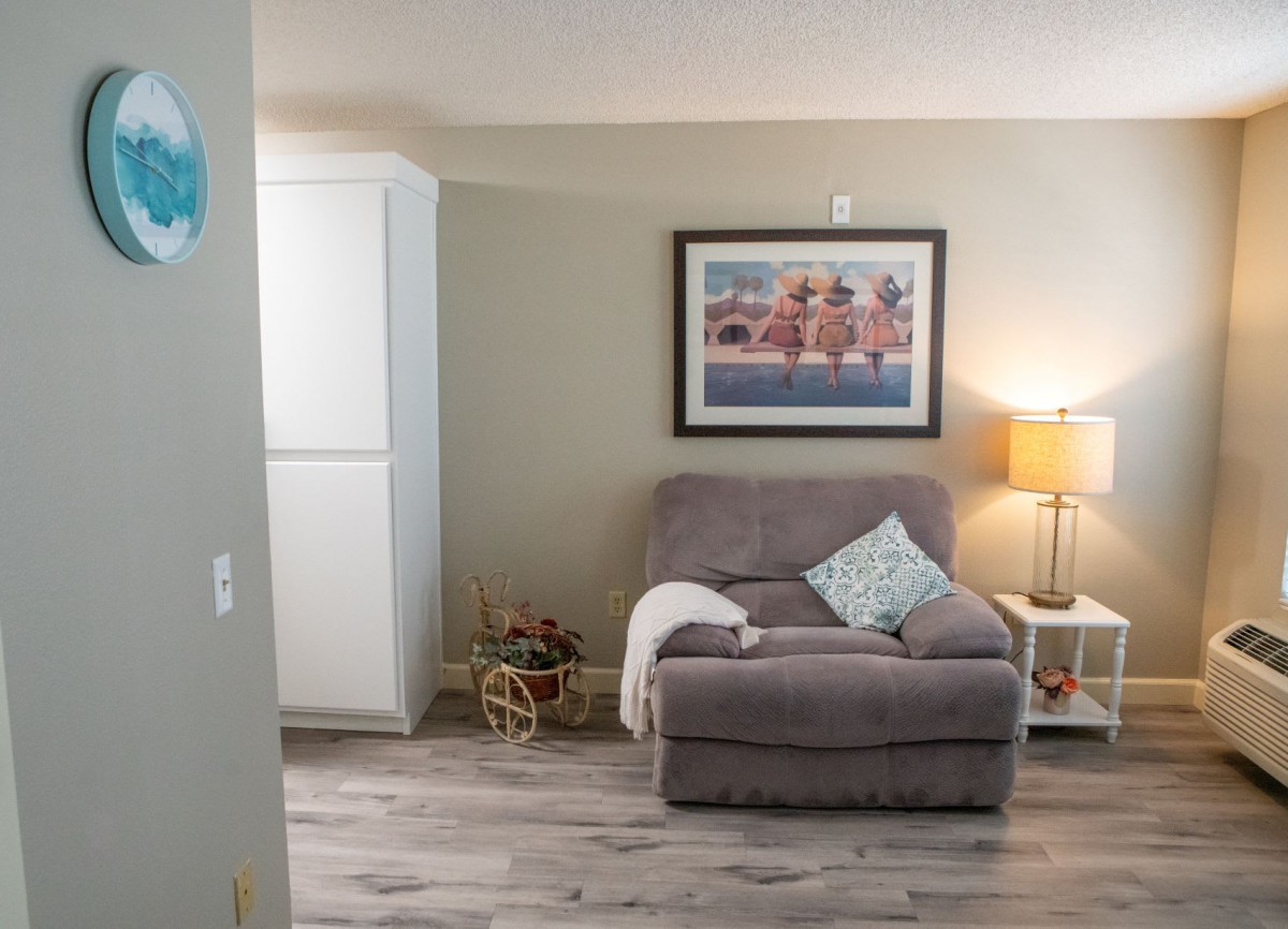 A cozy living room corner featuring a plush armchair with a pillow, a stylish lamp, and a decorative painting on the wall.