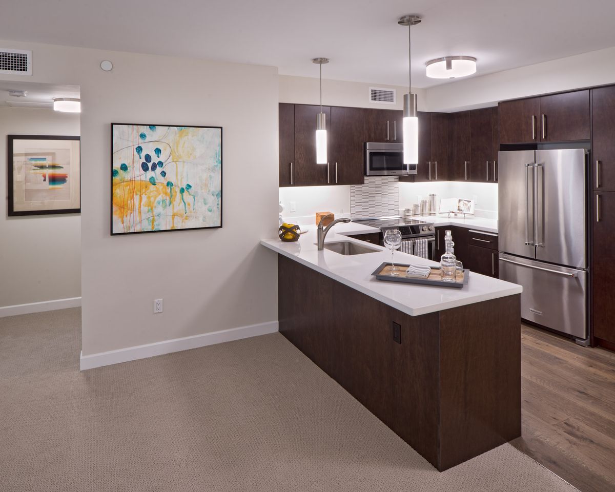 A modern kitchen with an open concept design featuring dark wood cabinets, a large island with seating, stainless steel appliances, and contemporary pendant lighting.