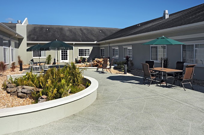 A sunny outdoor patio area with tables, chairs, and a landscaped garden bed.