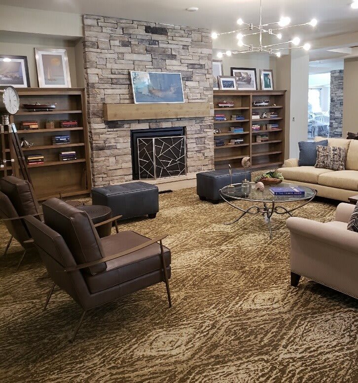 A cozy living room with a stone fireplace, bookshelves, and comfortable seating arranged around a central area rug.