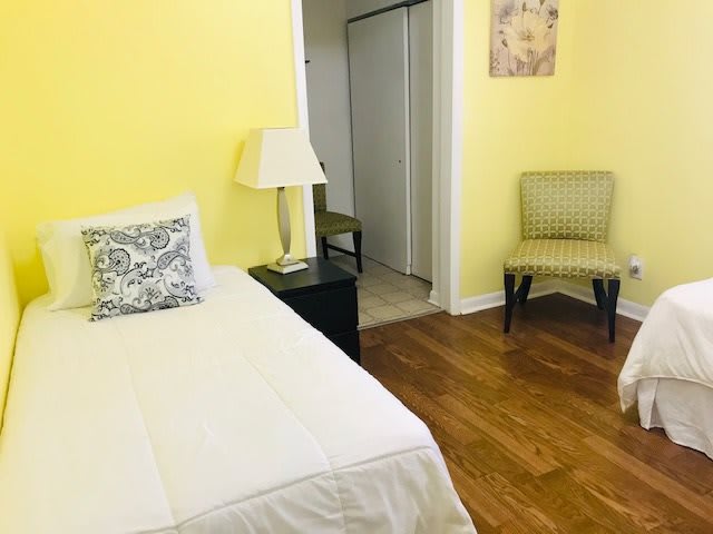 A cozy bedroom with yellow walls featuring a single bed, a lamp, and a chair on a wooden floor.