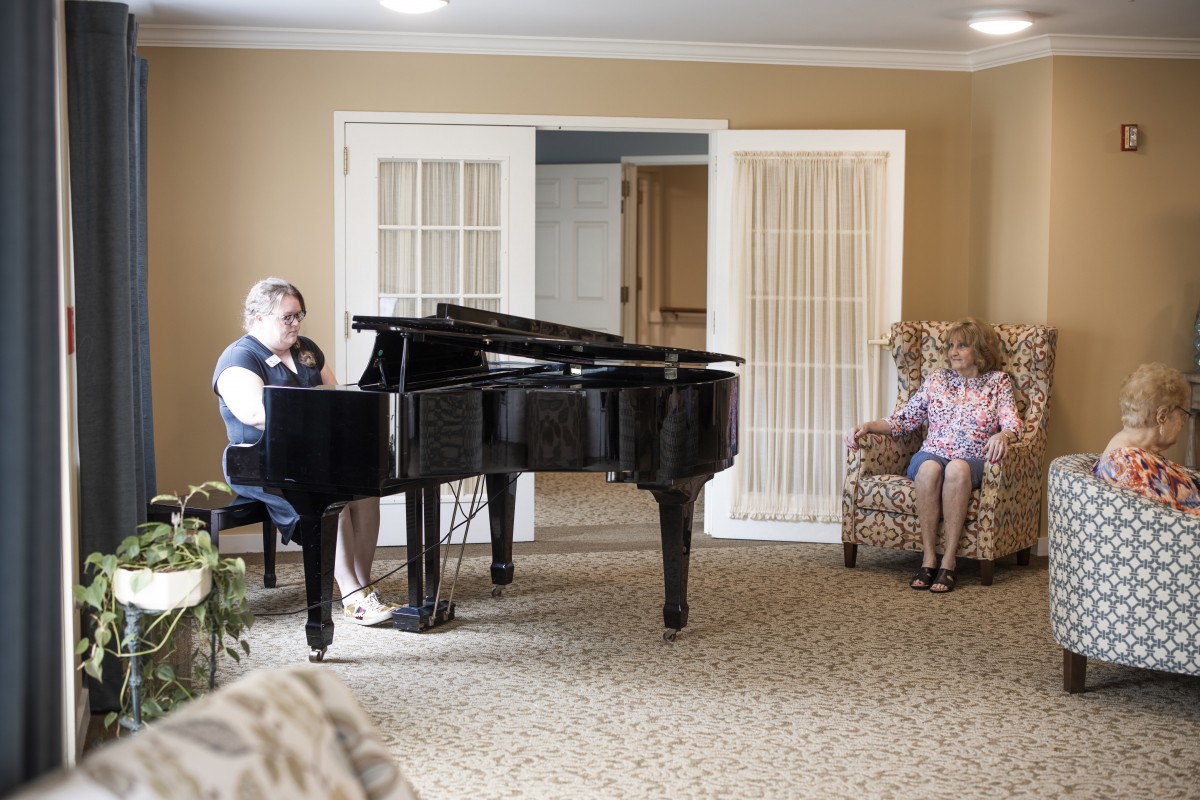 A person playing the piano in a cozy living room setting while another person sits and relaxes.