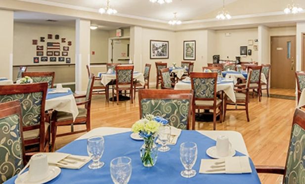 A cozy dining room setup with neatly arranged tables and chairs, featuring elegant table settings and a small bouquet of flowers on each table.